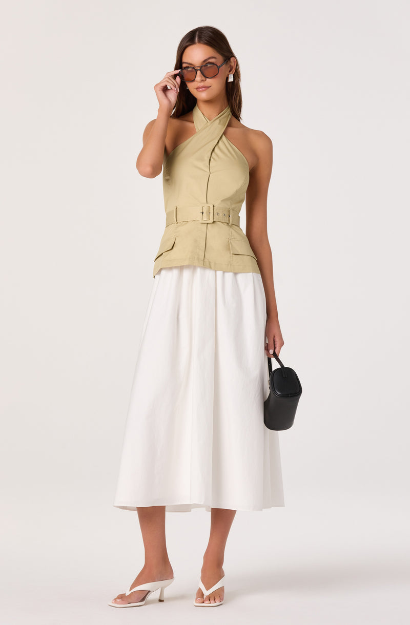 Model wearing a beige halter top with a buckle belt and wide-leg white skirt, holding a black handbag.