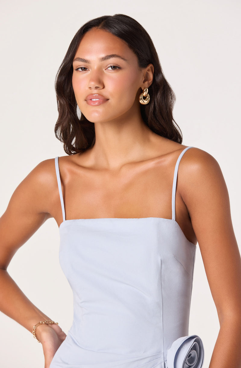 Woman in a white spaghetti strap dress with gold hoop earrings and a gold bracelet.