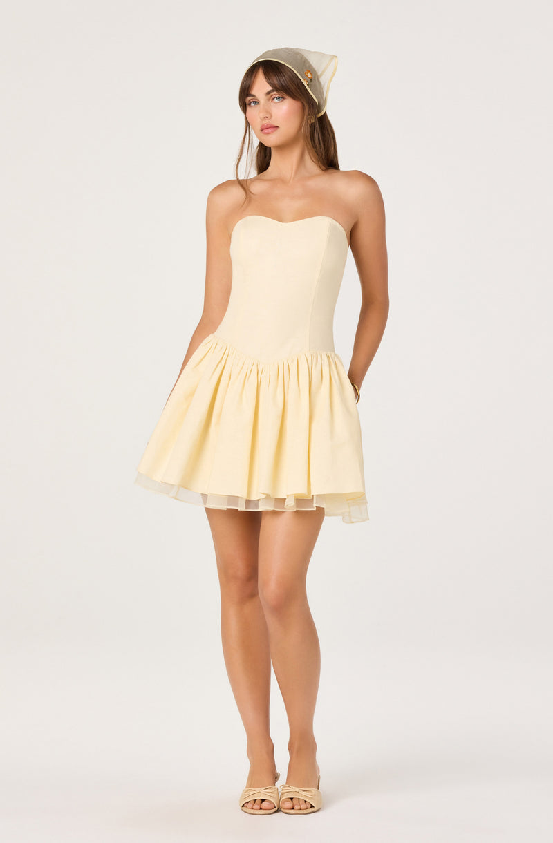 Woman in a strapless cream dress with a gathered, flared skirt and a beige hat.