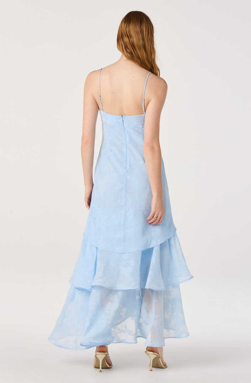 Woman in a light blue, layered, spaghetti strap dress with floral pattern and sheer fabric.