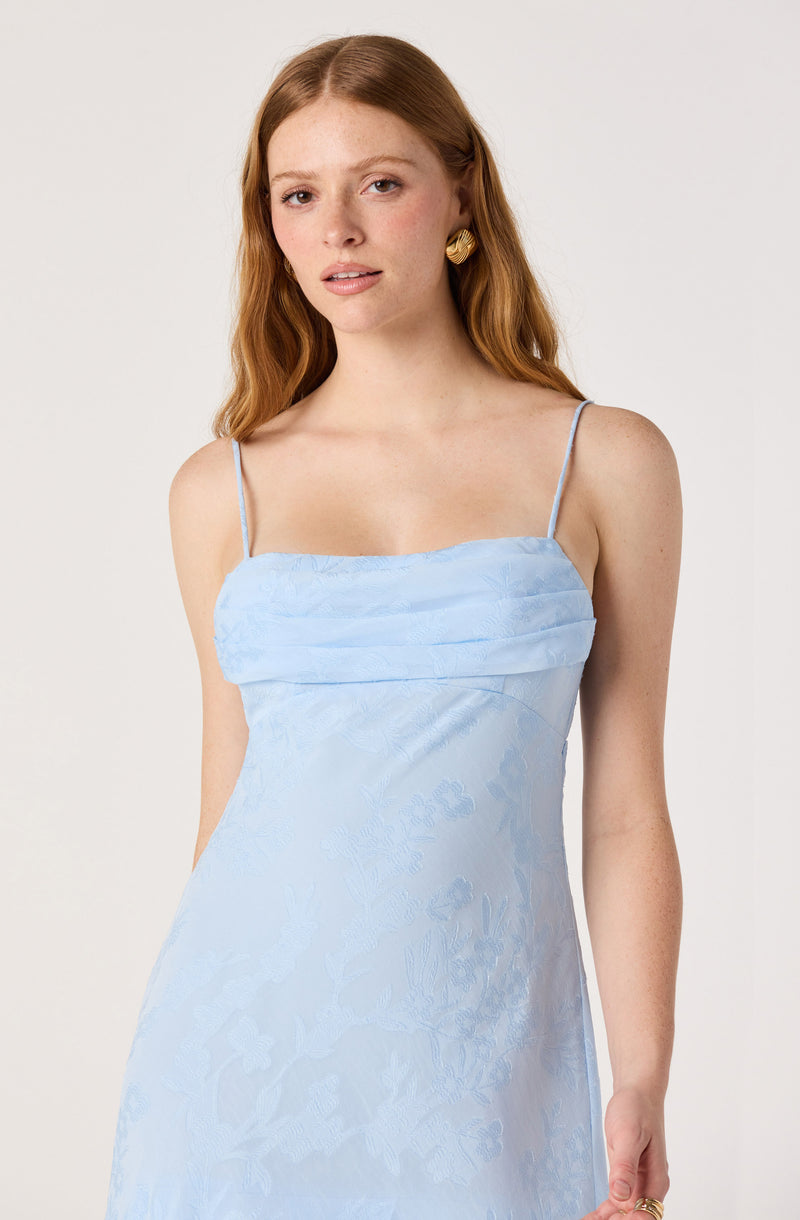 Woman in a light blue spaghetti strap dress with a textured bodice and floral pattern.
