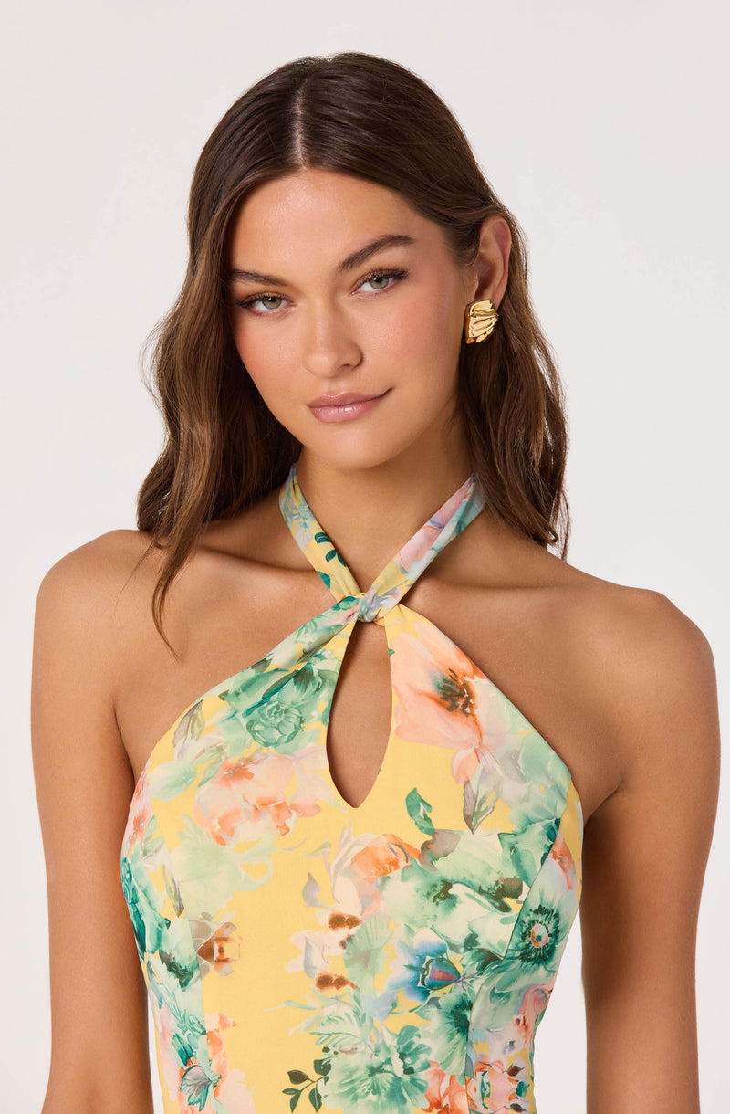 Woman wearing a halter top with a floral print in pastel colors and large gold earrings.