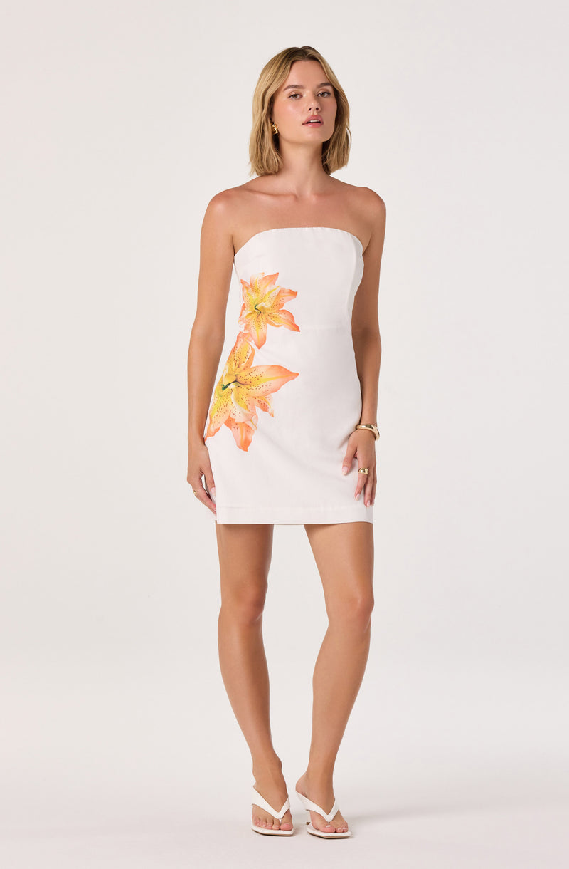 Woman in a strapless white dress with large orange and yellow floral print, white high-heeled sandals.