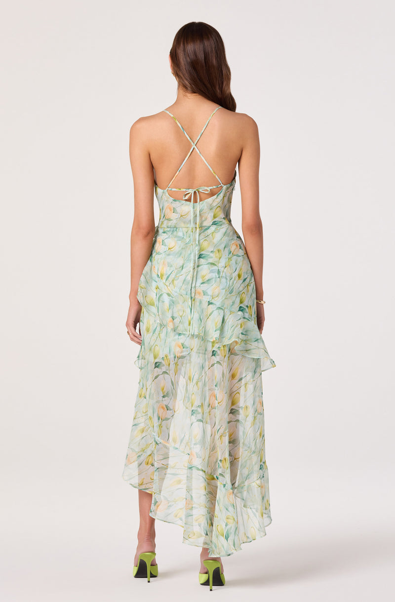 Back view of a woman wearing a flowing, pastel-colored floral dress with thin, criss-cross straps.