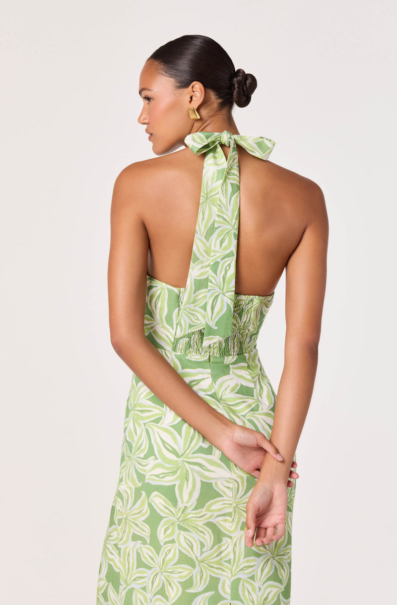 Back view of a woman wearing a green and white patterned halter dress with a bow tie at the neck.