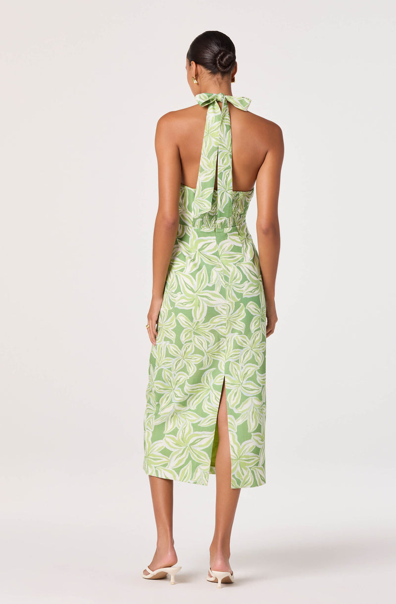 Back view of a woman wearing a green and white patterned halter dress with a slit.