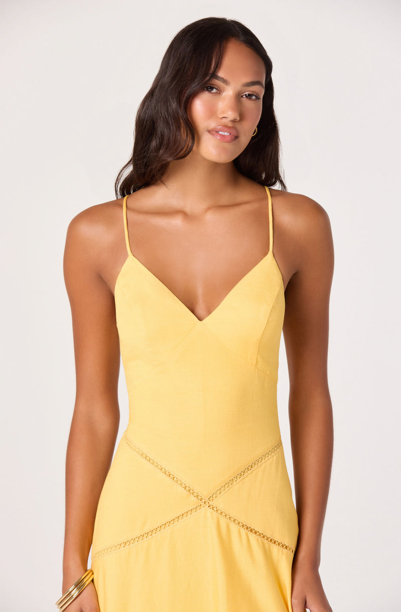 Woman in a yellow spaghetti strap dress with V neckline and decorative cutouts.