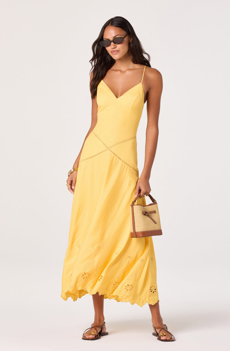 Woman in a yellow sundress with spaghetti straps, floral embroidery at the hem, and sunglasses.