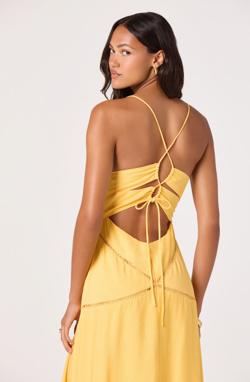 Woman in yellow spaghetti strap top with open back and tie bow, matching yellow skirt with cutout details.