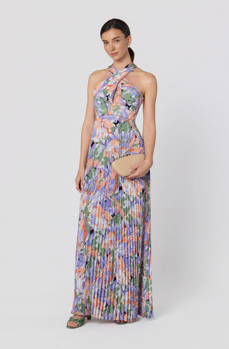Woman in a sleeveless, colorful floral maxi dress with a halter-style neckline and pleated skirt.