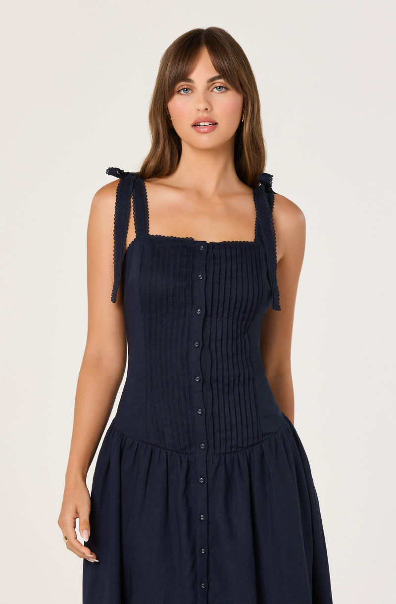 Woman wearing a navy sleeveless dress with vertical ribbing and shoulder ties.