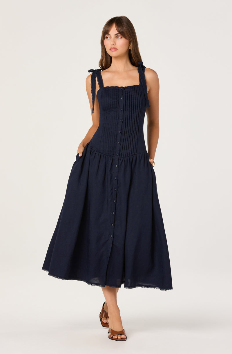 Women in navy sleeveless dress with tied shoulder straps and button-front pleated skirt.