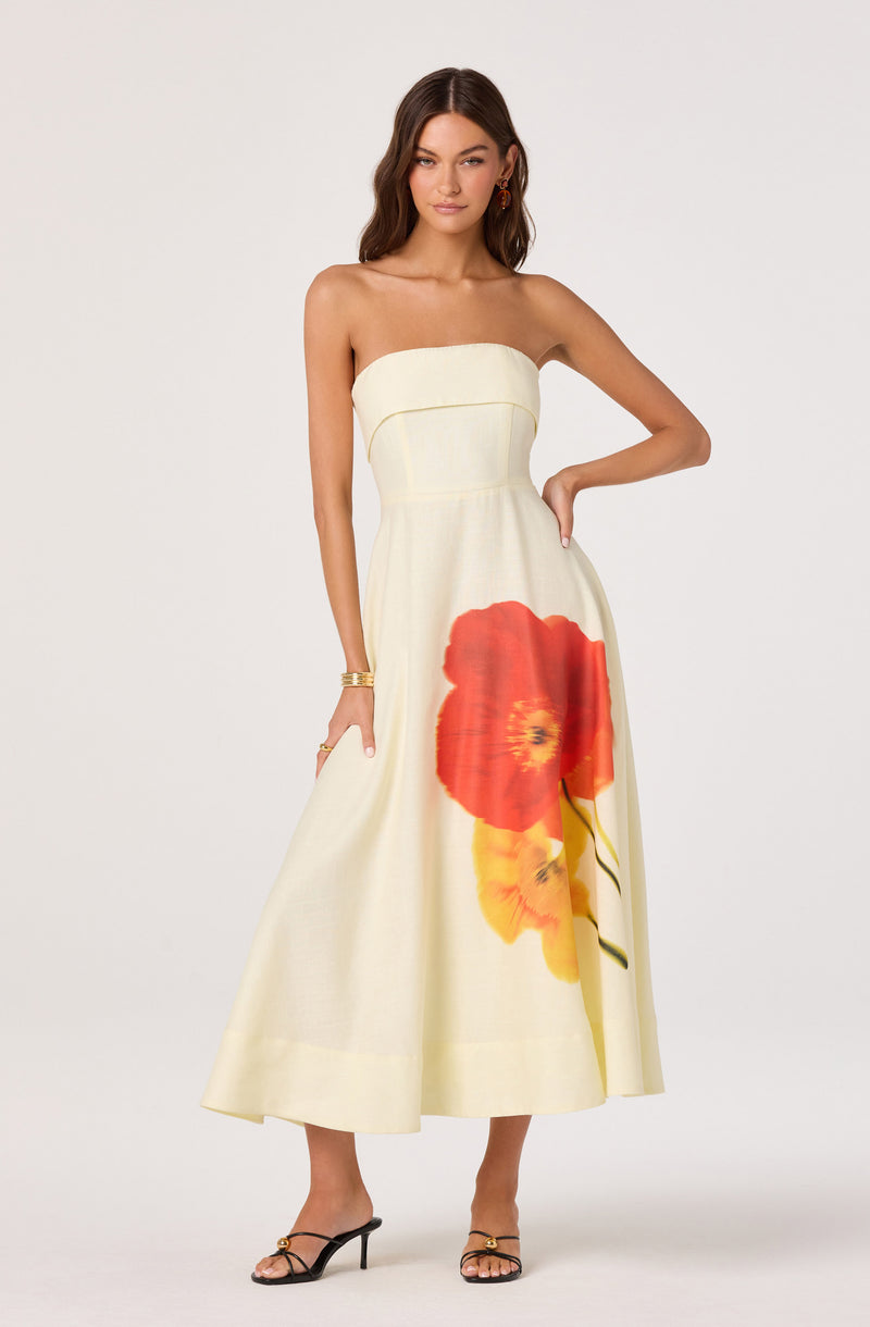 Strapless cream dress with large red and yellow floral print, midi length, held with gold high-heeled sandals.