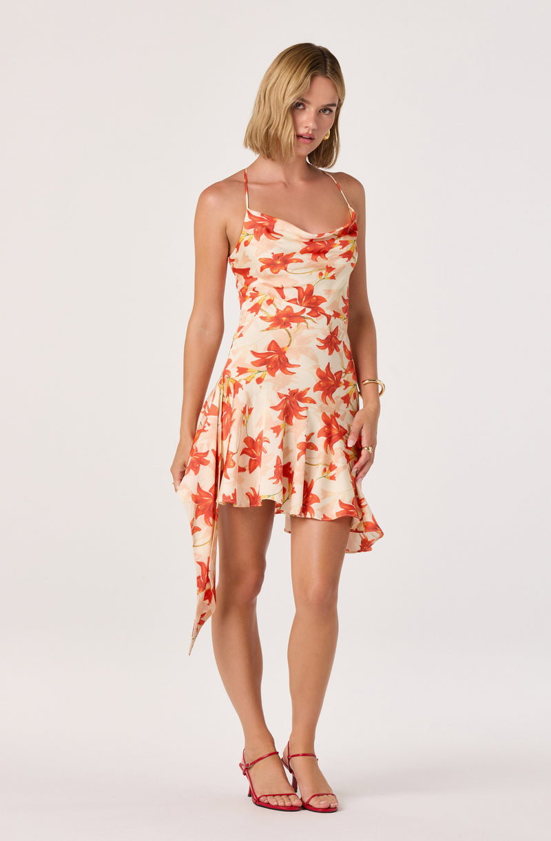Woman in a floral, sleeveless, orange and cream dress with thin straps, paired with matching red heels.
