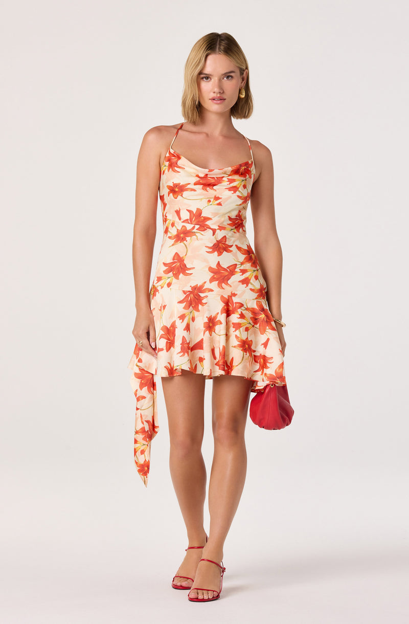 Woman in floral cream and orange dress with spaghetti straps, holding a red purse.
