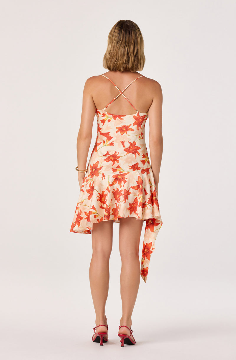 Woman in a sleeveless, floral, spaghetti strap dress with a ruffled skirt and a handkerchief hem.