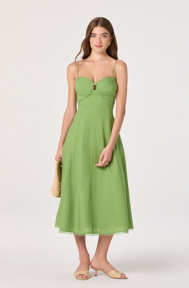 Woman wearing a green midi dress with spaghetti straps and decorative trim details.