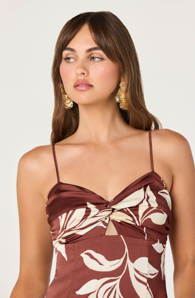 Woman wearing a brown dress with thin straps and a floral pattern, large gold earrings.