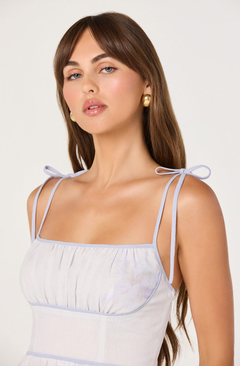 Woman in a white sleeveless top with light purple shoulder straps tied in bows.