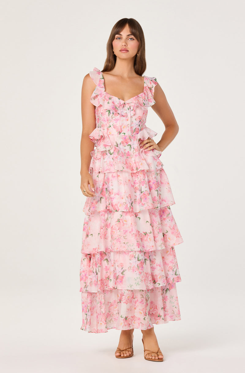 Woman wearing a pink floral tiered ruffle dress with wide shoulder straps and sandals.
