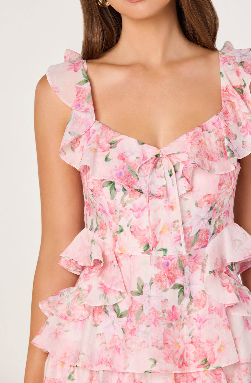 Woman wearing a pink floral ruffled dress with a bow at the neckline.
