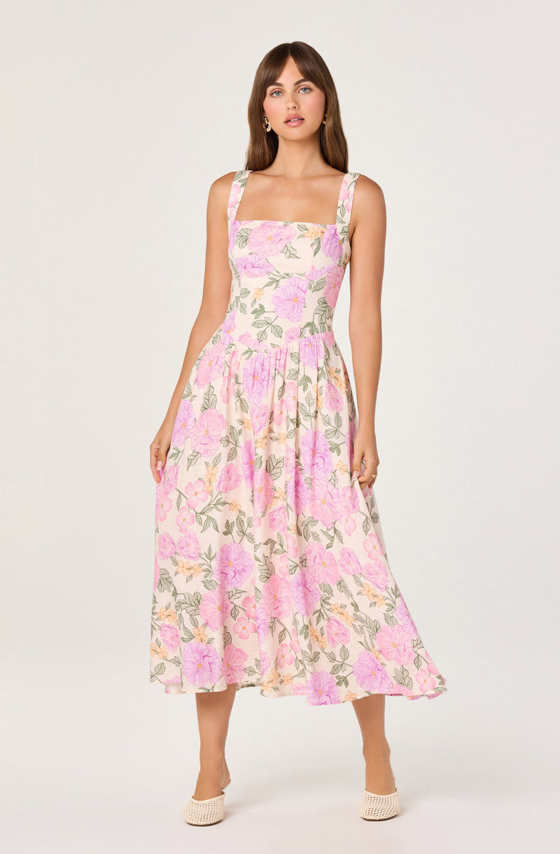 Woman in a sleeveless, floral, midi-length dress with pink, purple, and green pattern.