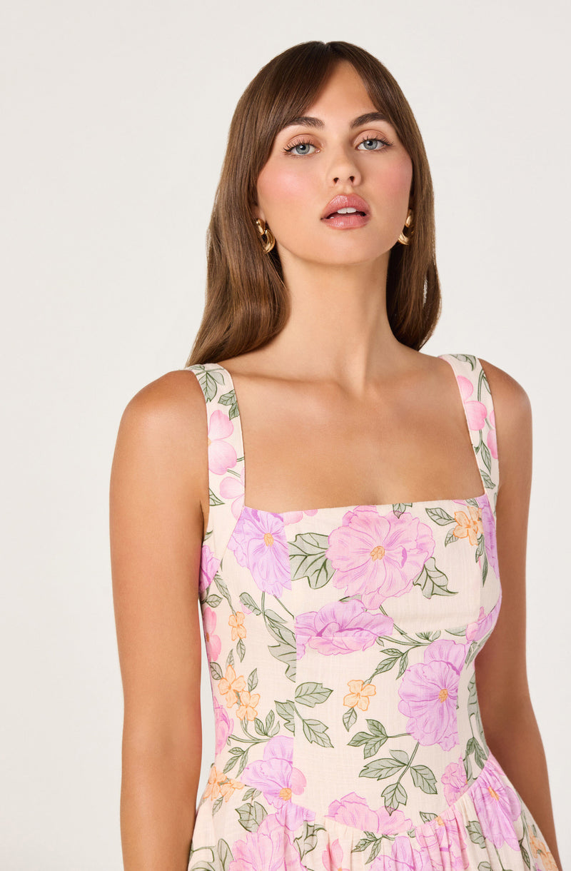 Woman in a sleeveless dress with pink, purple, orange flowers and green leaves.