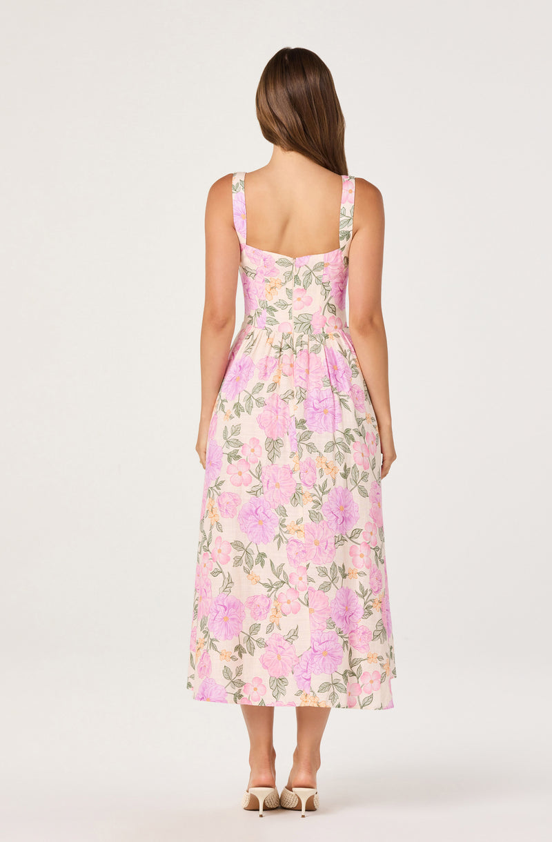Woman wearing a sleeveless, floral-patterned pink and beige dress with square neckline.