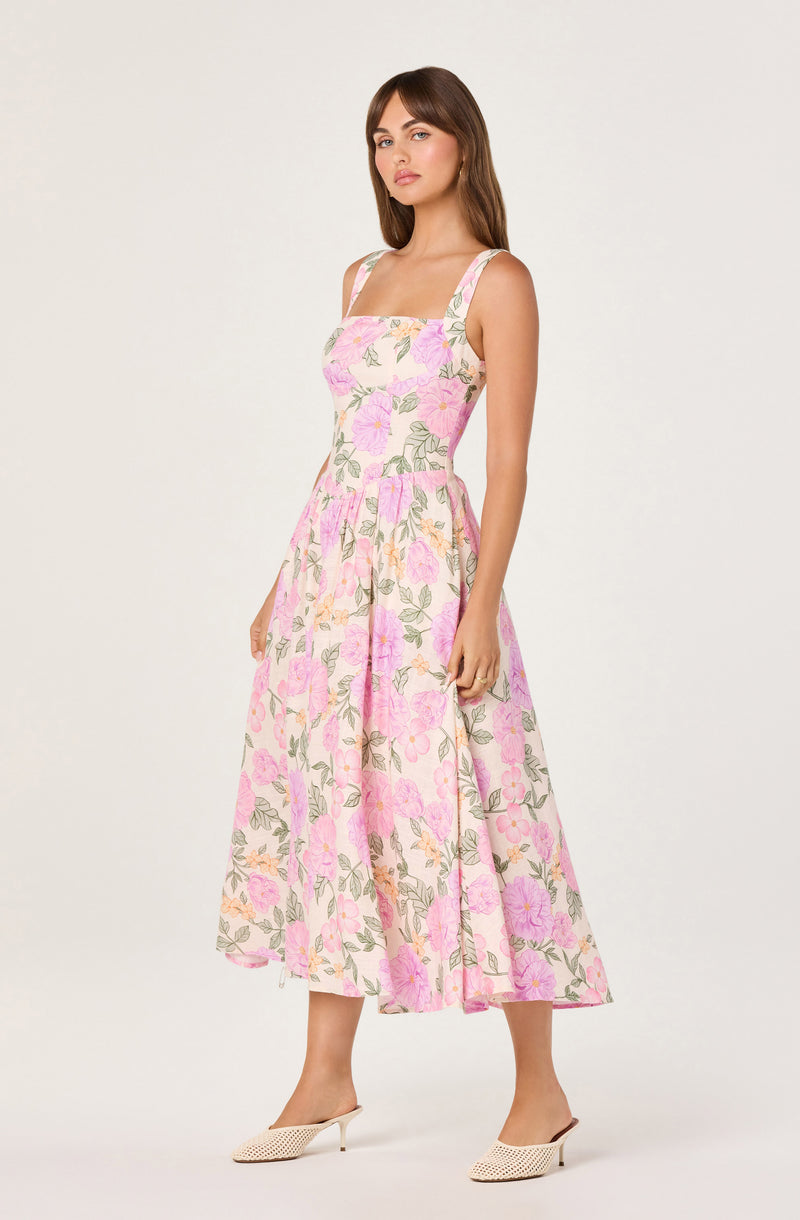 Woman wearing a sleeveless, floral pink and green dress with a square neckline.