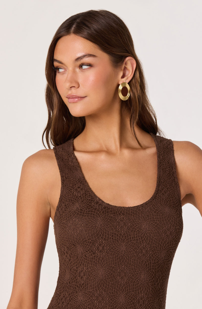 Woman wearing a textured brown sleeveless top with large gold hoop earrings.