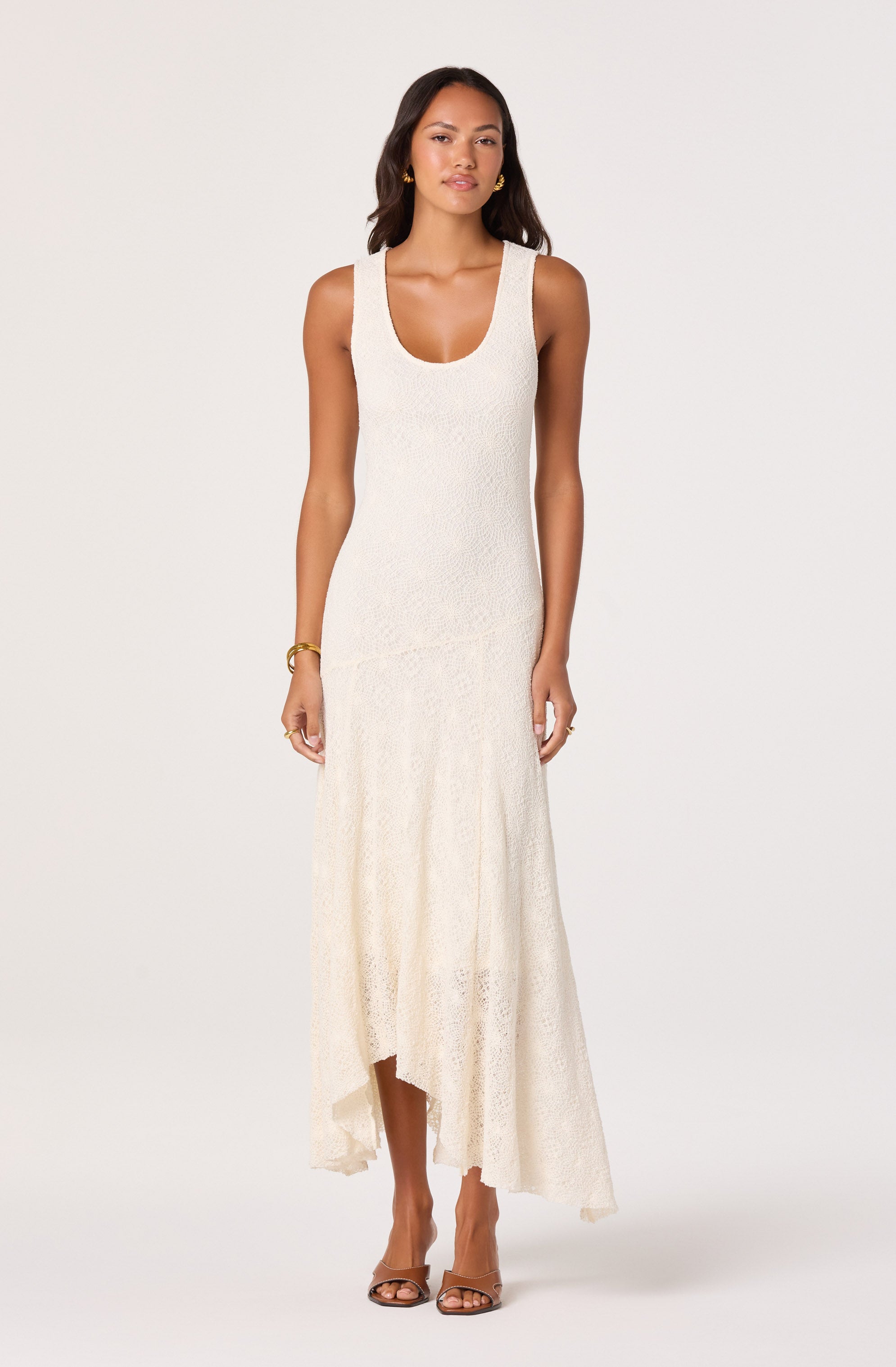 Woman in cream sleeveless maxi dress with a scoop neckline and lace-like texture, paired with sandals and gold jewelry.