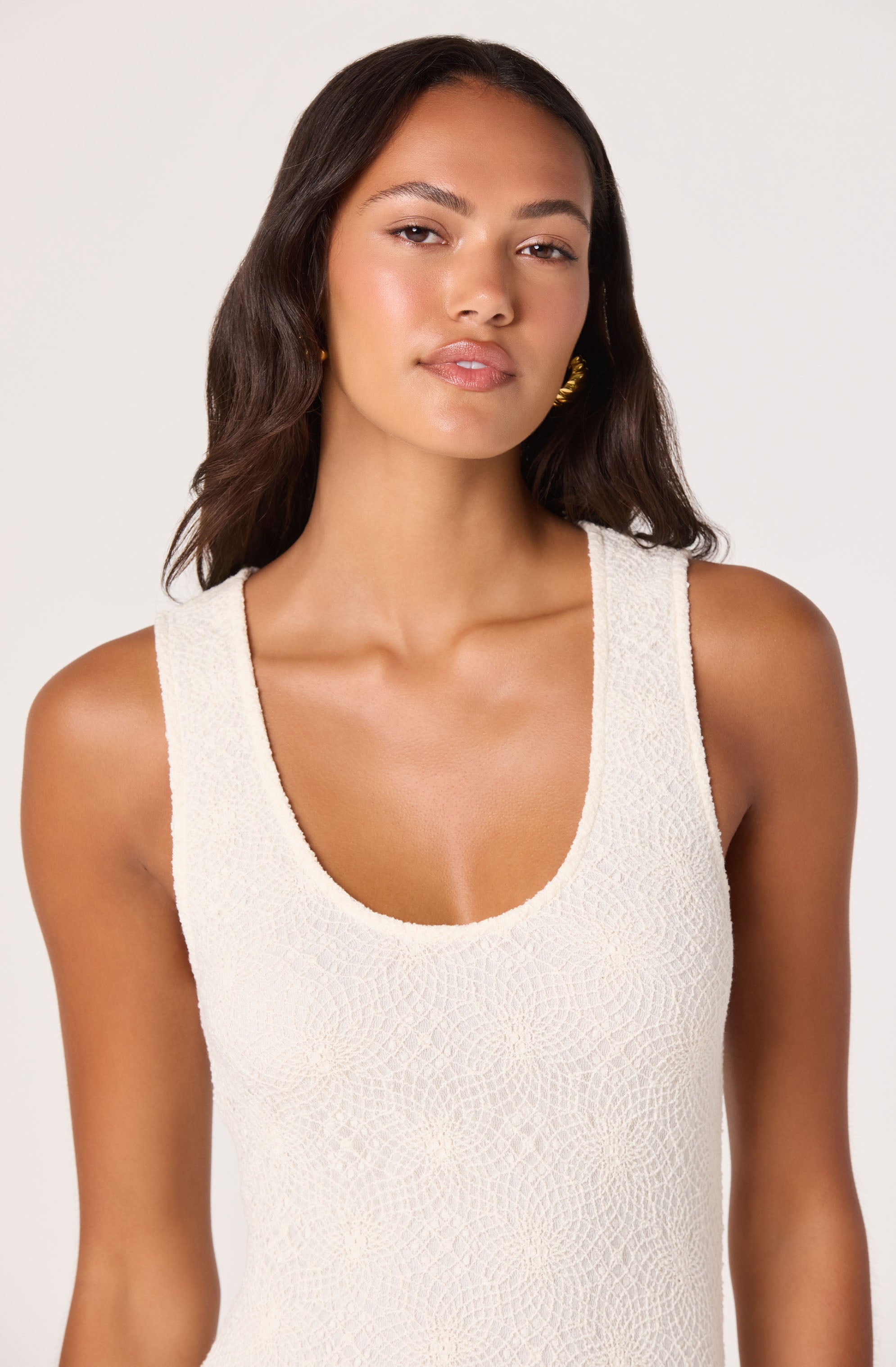 Woman wearing a sleeveless, textured white top with a scoop neckline.