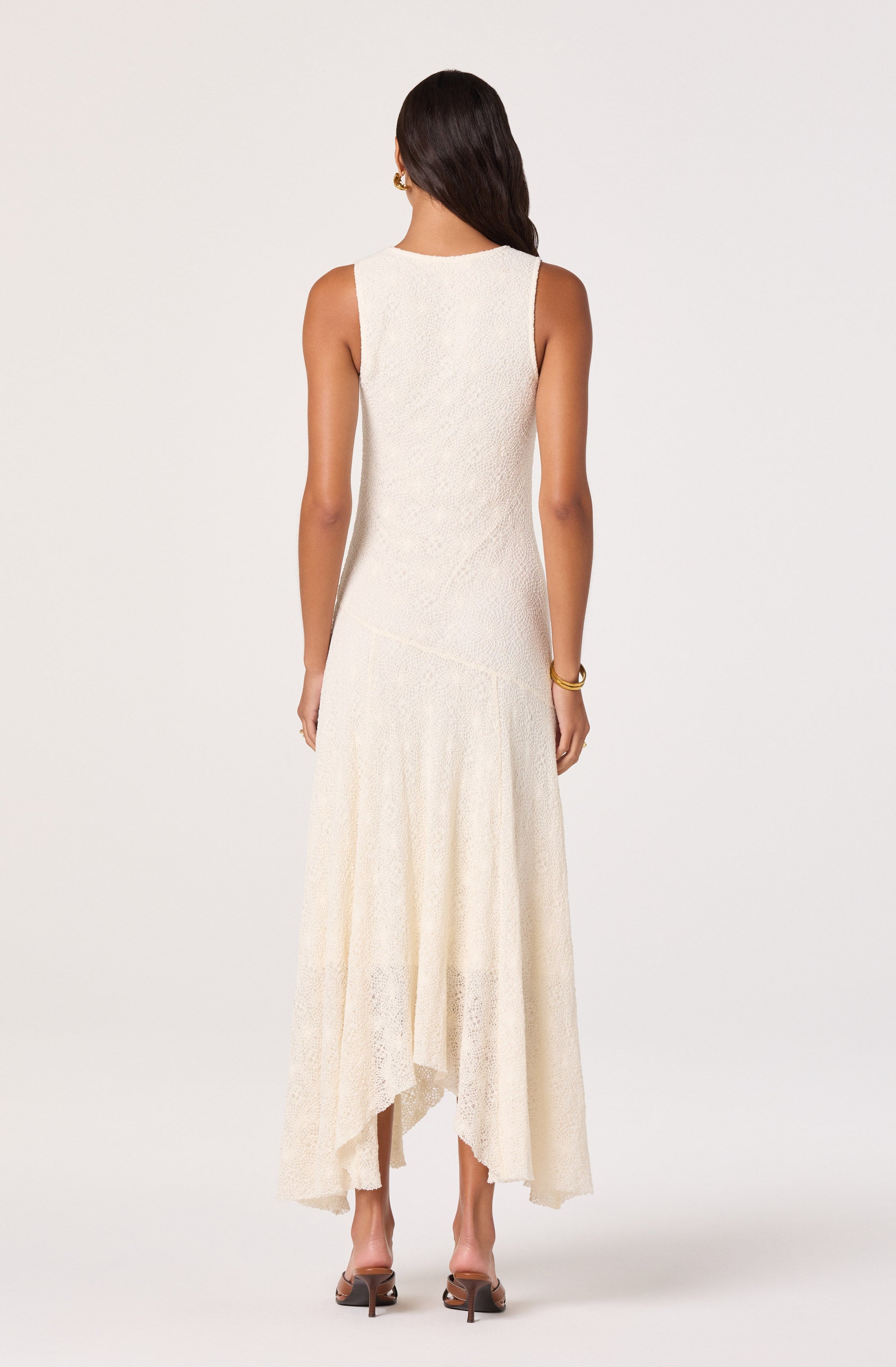 Woman in a sleeveless, cream, lace maxi dress, facing away.