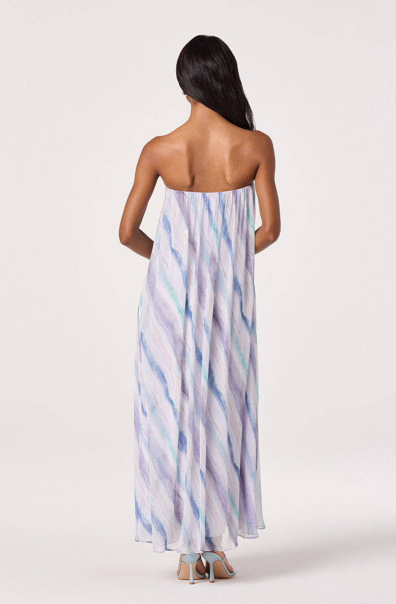 Woman wearing a strapless, flowy, pastel-colored maxi dress with a watercolor pattern.