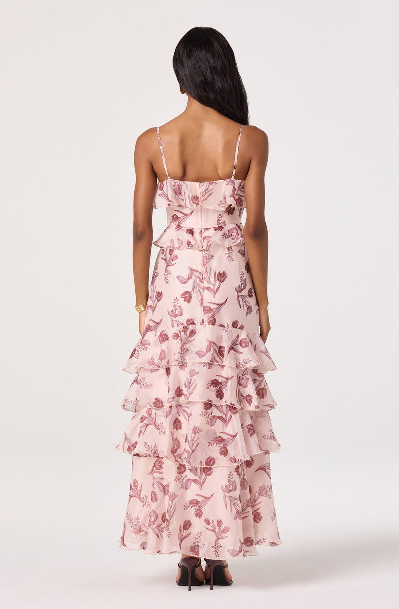 Back view of a woman in a pink, floral, tiered maxi dress with spaghetti straps.