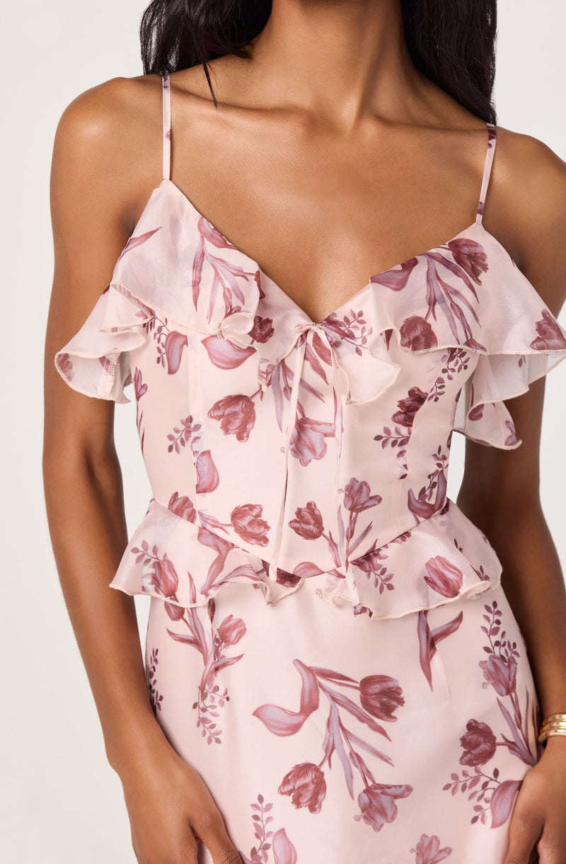 Woman wearing a pink floral dress with ruffled straps and layered ruffles at the waist.