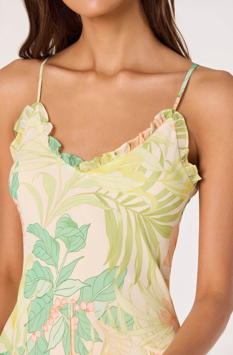 Woman wearing a sleeveless dress with a leafy botanical print and ruffled neckline.