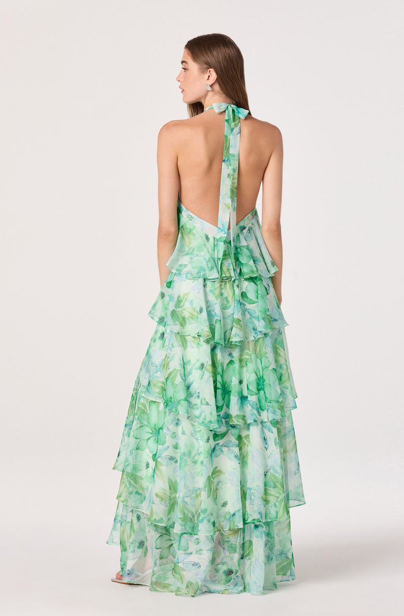 Back view of a woman in a long, sleeveless, green floral tiered dress with a halter neck tie.