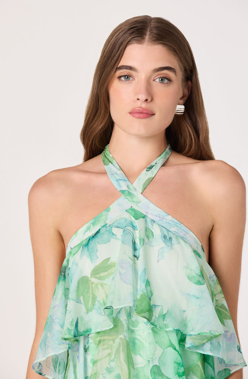 Woman in a green and white floral halter-top dress with ruffles and a crisscross neckline.