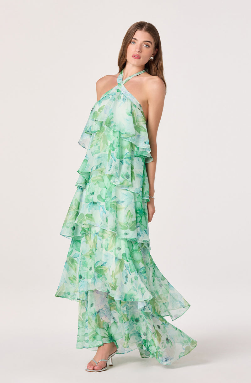 Woman wearing a green floral halter maxi dress with ruffled layers, sheer fabric, and open-toe heels.