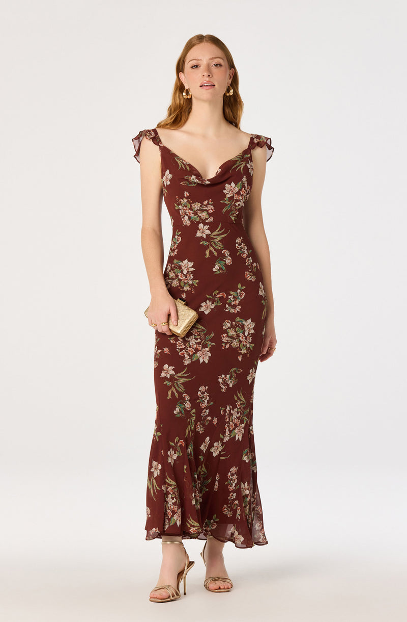 Woman in a long, floral burgundy dress with ruffled shoulder details, holding a gold clutch.