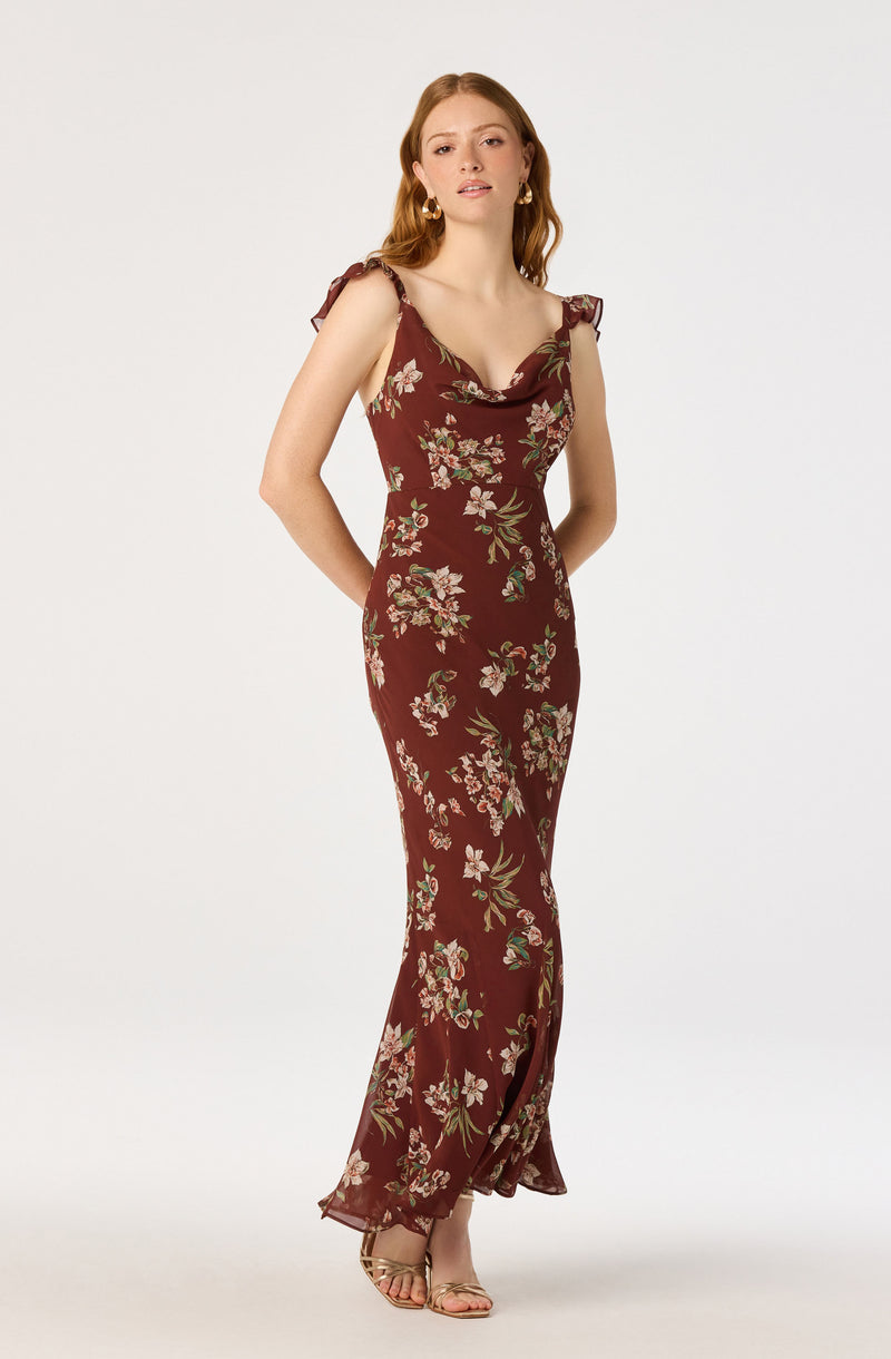 Woman in a long, burgundy floral dress with ruffled shoulder straps and a slit.