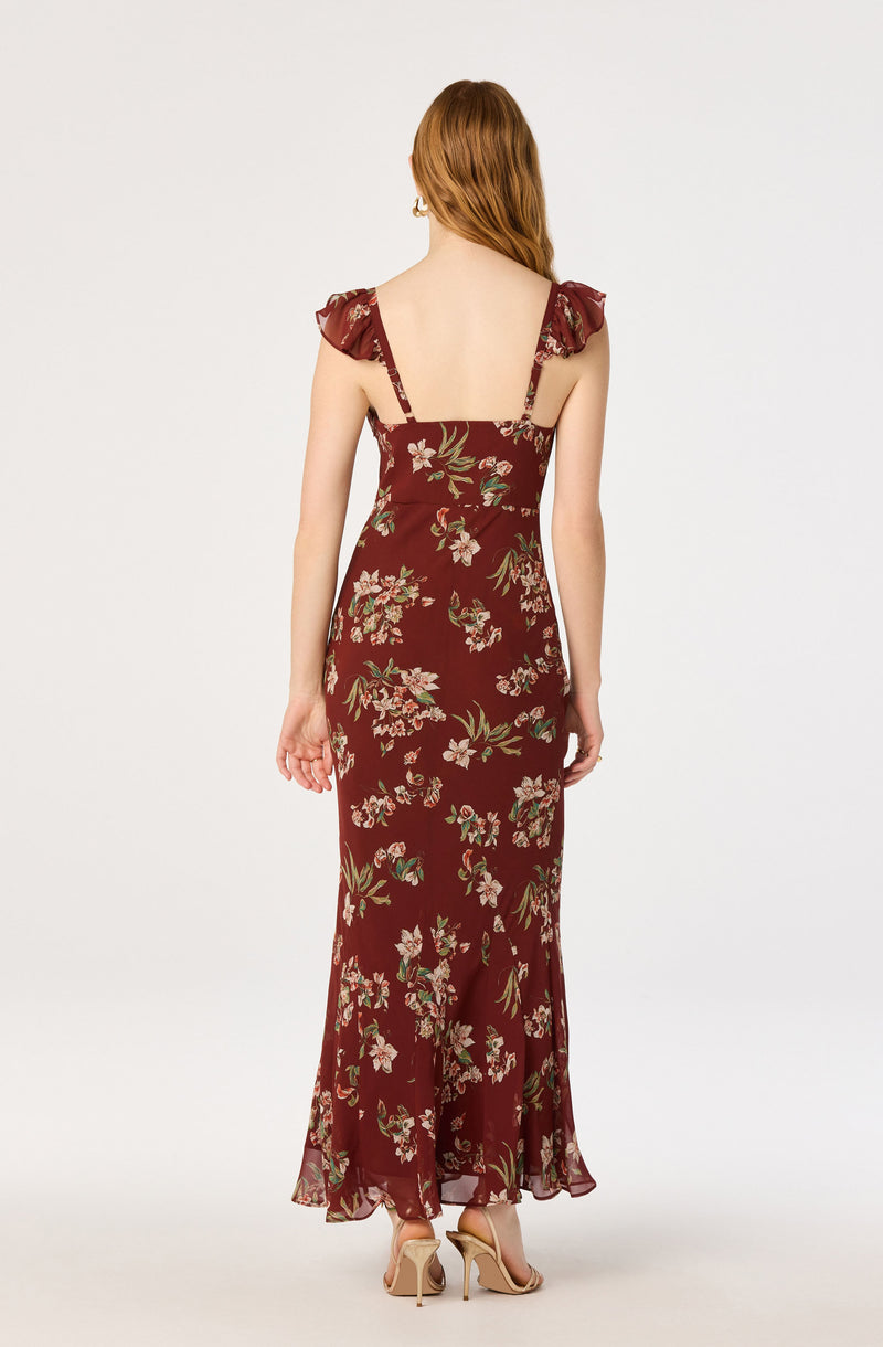 Back view of a woman in a long, floral burgundy dress with ruffled shoulder details.