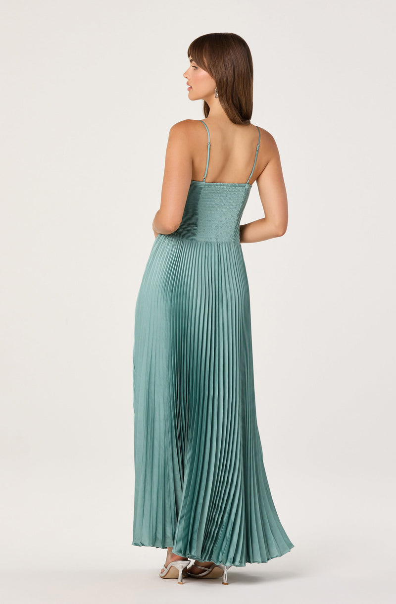 Woman in a teal pleated maxi dress with thin shoulder straps and open back.