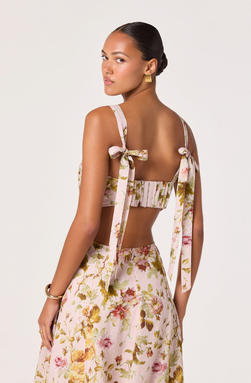 Woman wearing a floral print crop top with tied shoulder straps and matching high-waisted skirt.