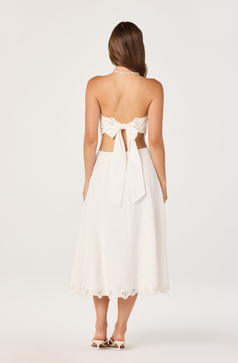 Woman in a white strapless top and long white skirt, back view.