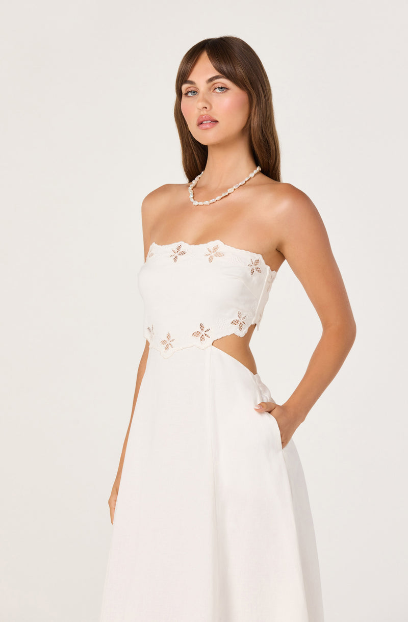 Woman in a white strapless dress with embroidered floral details and cutouts, wearing a pearl necklace.