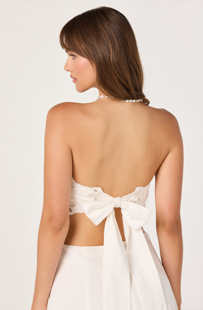 Backless white dress with a large bow and lace details on the top.