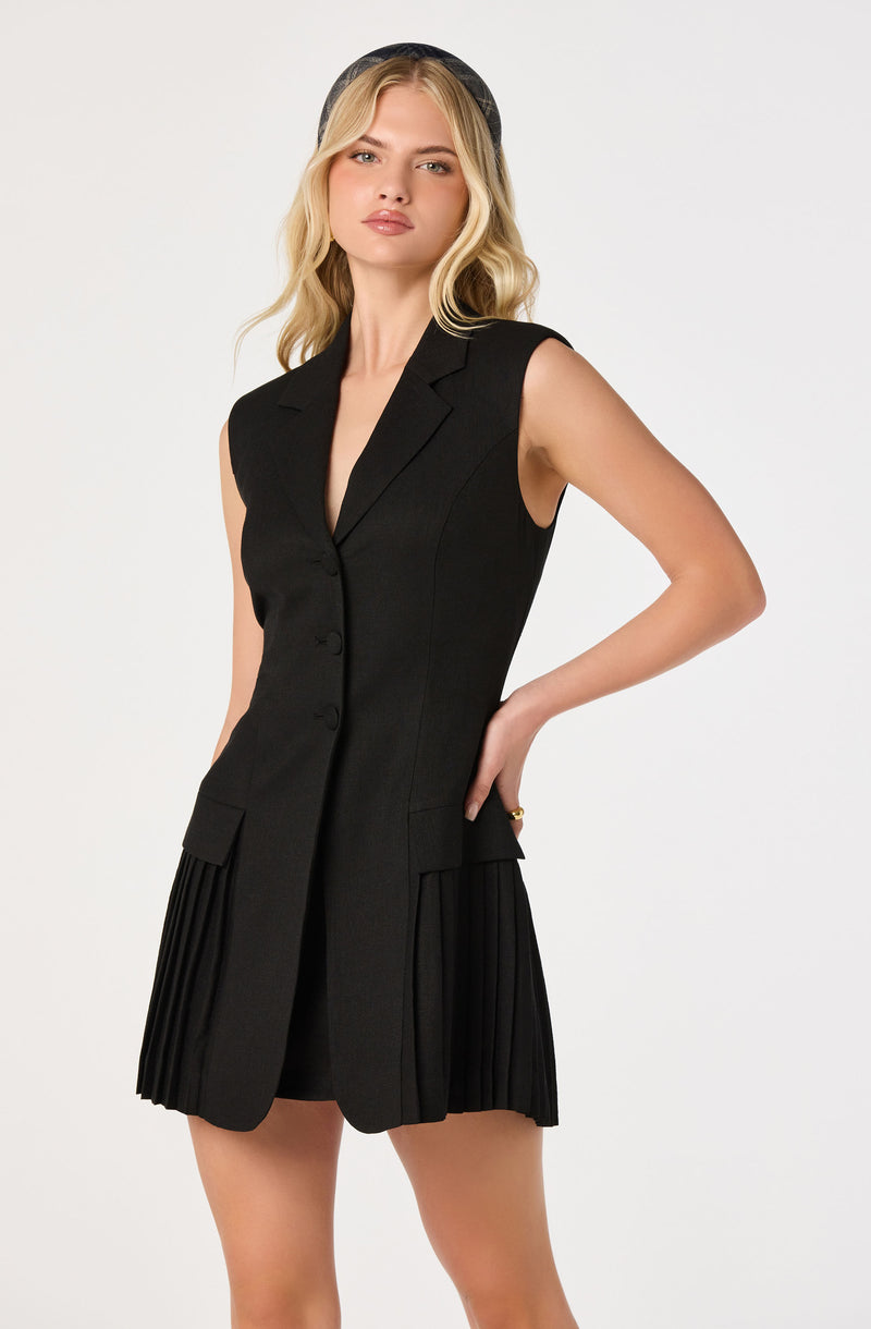 Woman wearing a sleeveless black blazer dress with pleated skirt panels.