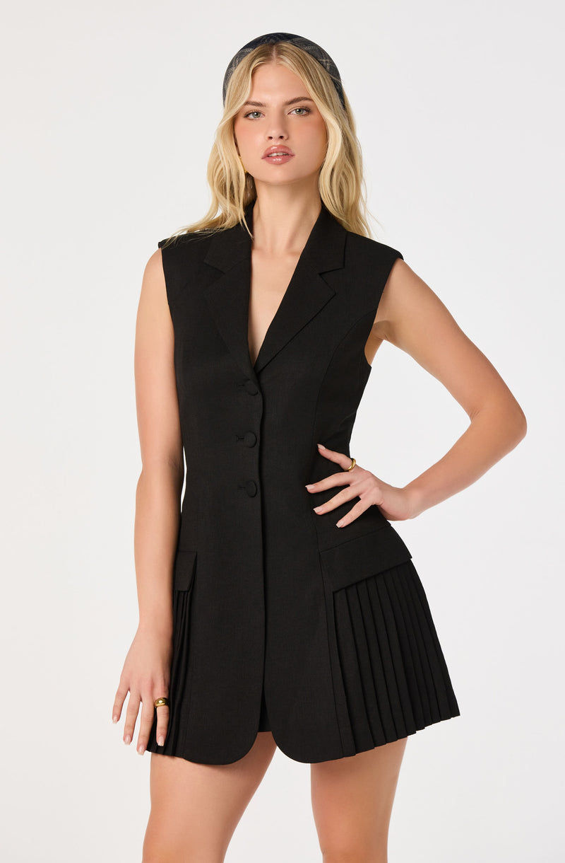 Blonde woman in a sleeveless black blazer with pleated black shorts and a black hat.